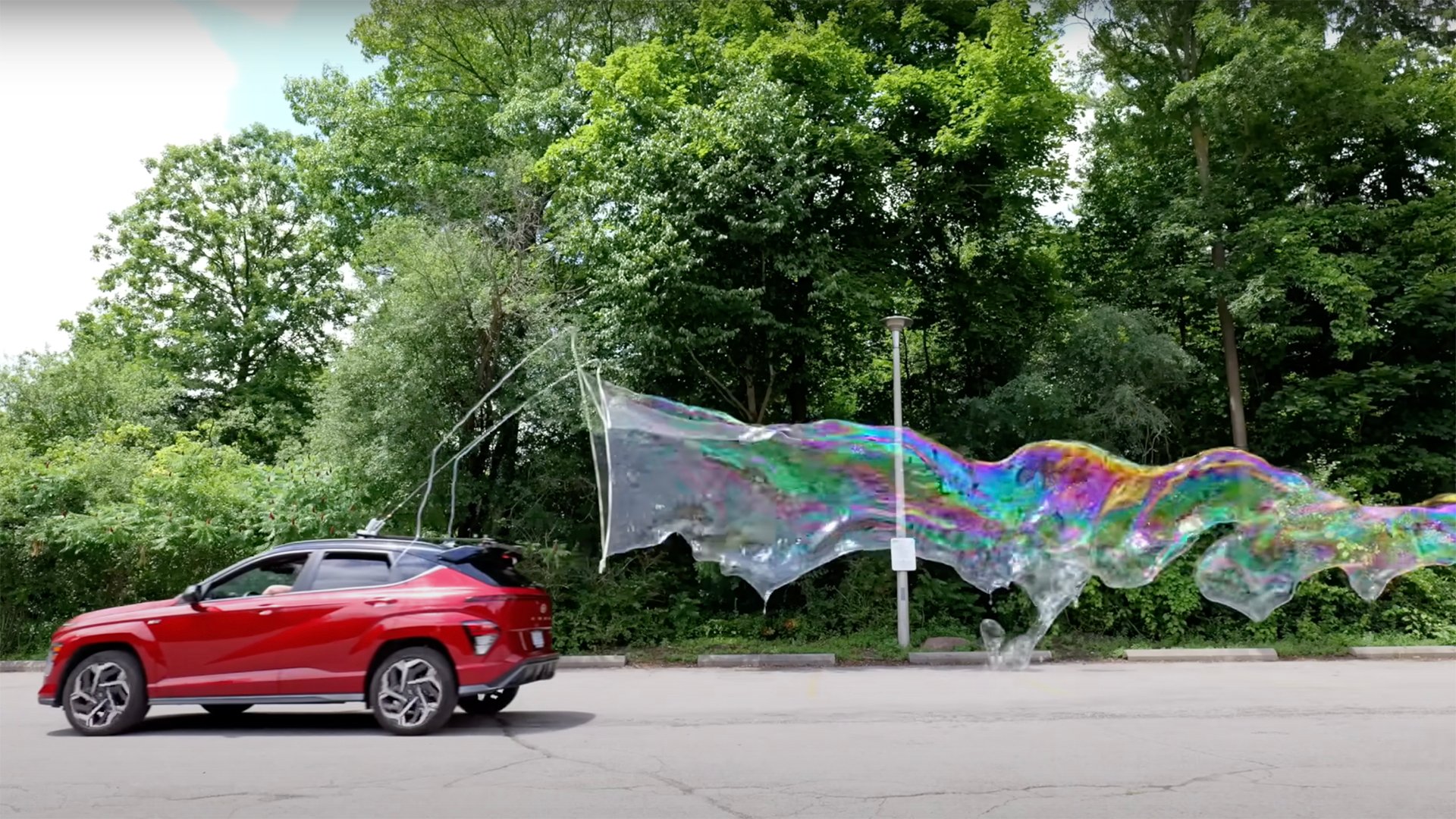 A red car with a DIY bubble making machine mounted on top creating a large bubble