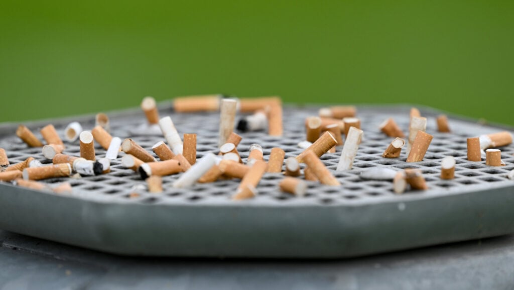 Cigarette butts stuck on a garbage can with an ashtray.