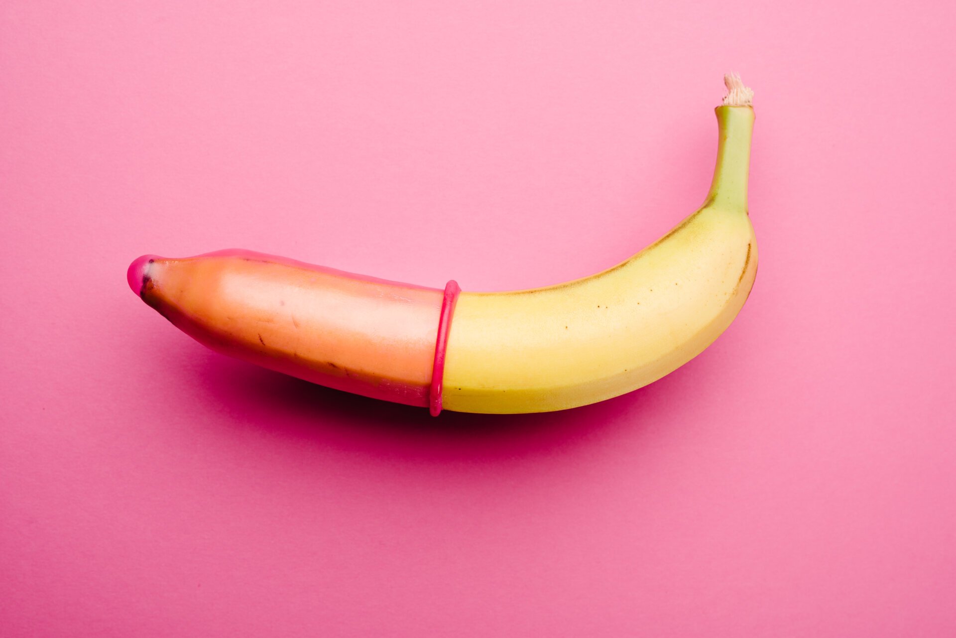 Pink,condom,on,fresh,yellow,banana,in,front,of,pink